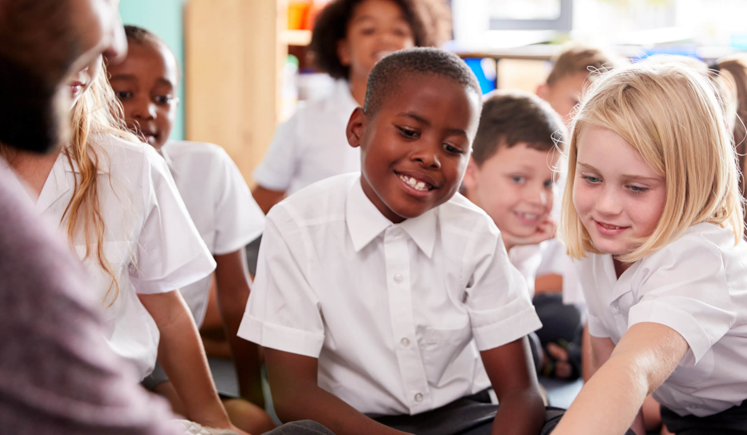 Students in classroom smiling and pointing at item that teacher is holding