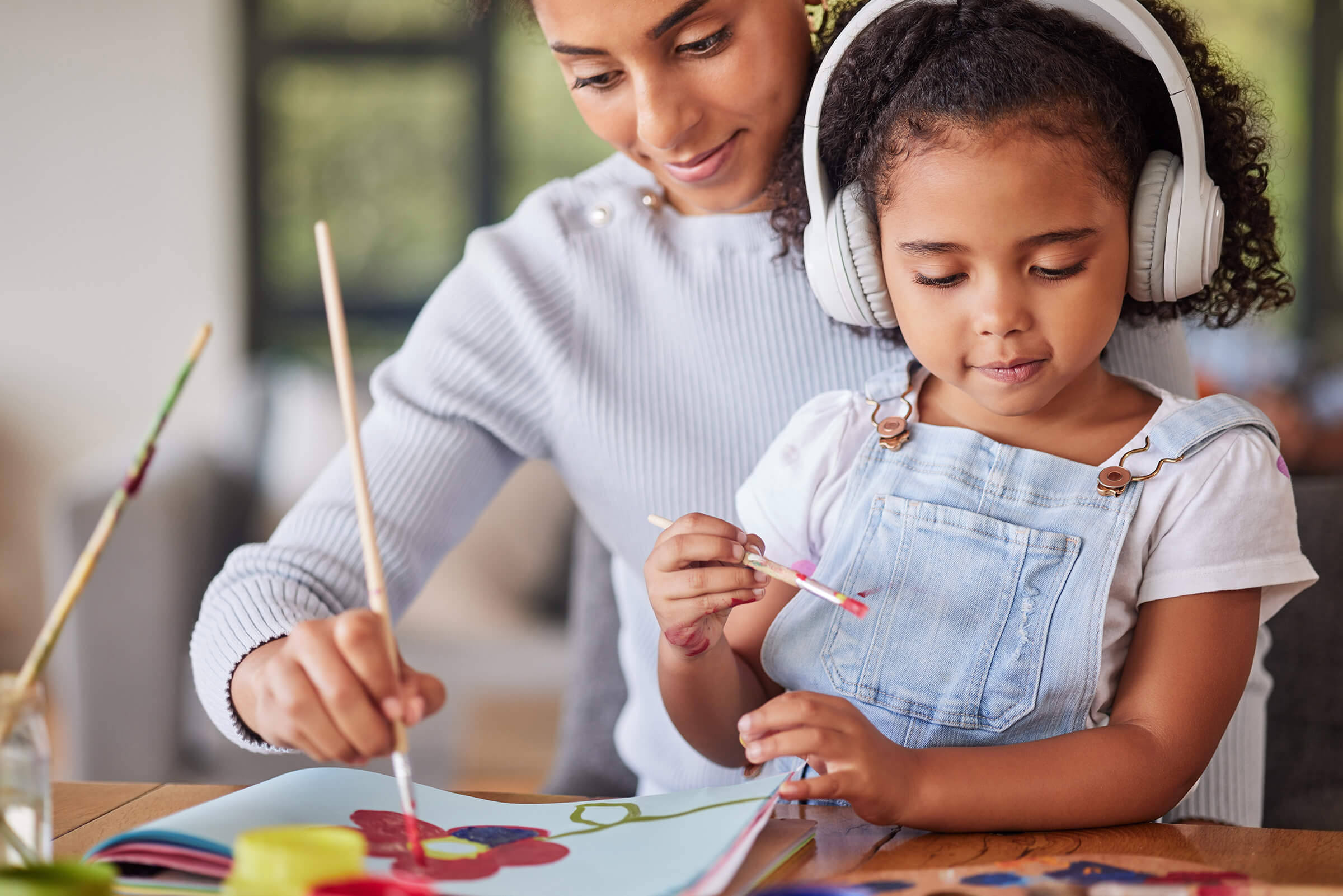 Child wearing headphones while sitting on adults lap and painting