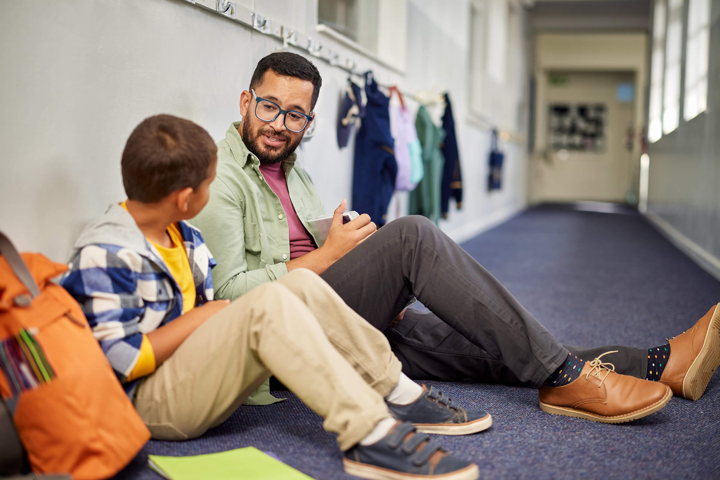Student and teacher sitting in hallway leaning against wall